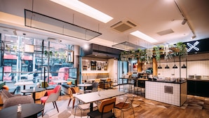 A modern cafe with a mix of seating options, including tables and chairs, and a visible kitchen area. - ibis Belfast City Centre (Belfast)