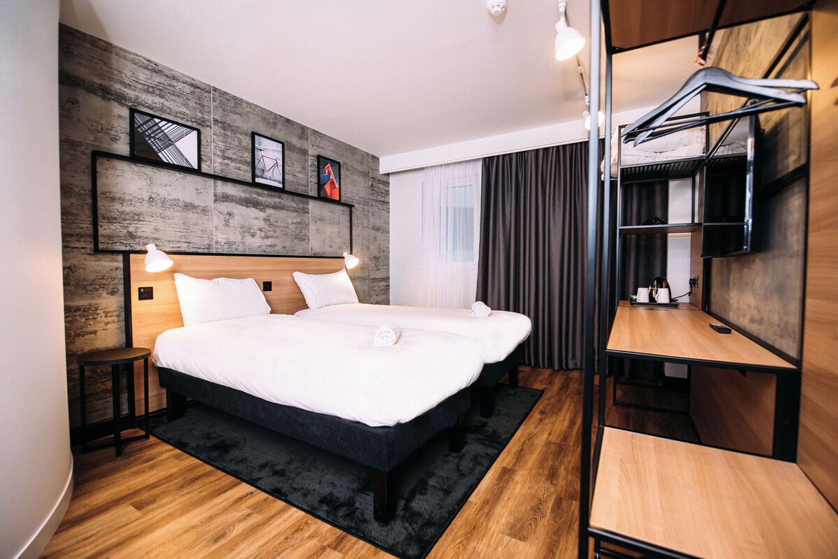 A modern hotel room with a large bed, bedside tables, a desk, and a TV.