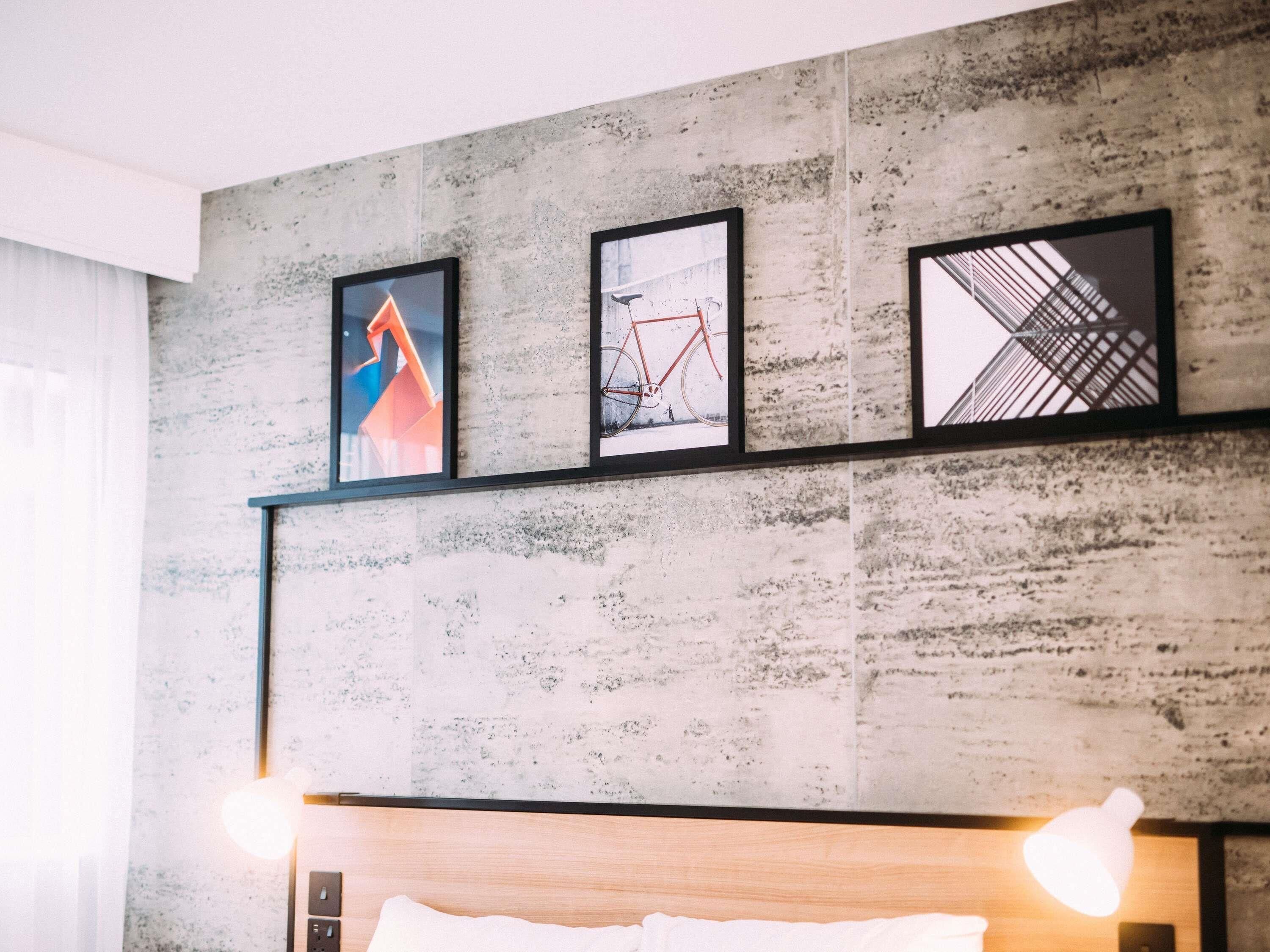 Una habitación moderna con pared de concreto, cabecera de madera y tres cuadros enmarcados.