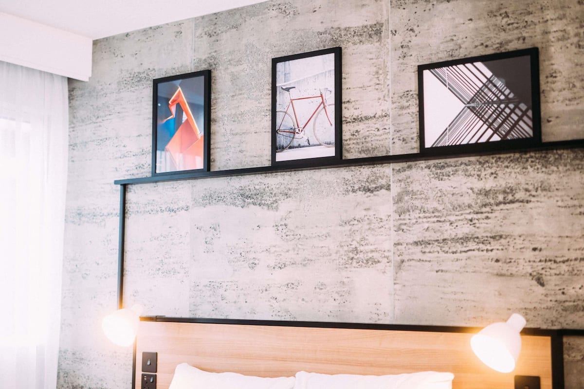 Una habitación moderna con pared de concreto, cabecera de madera y tres cuadros enmarcados.