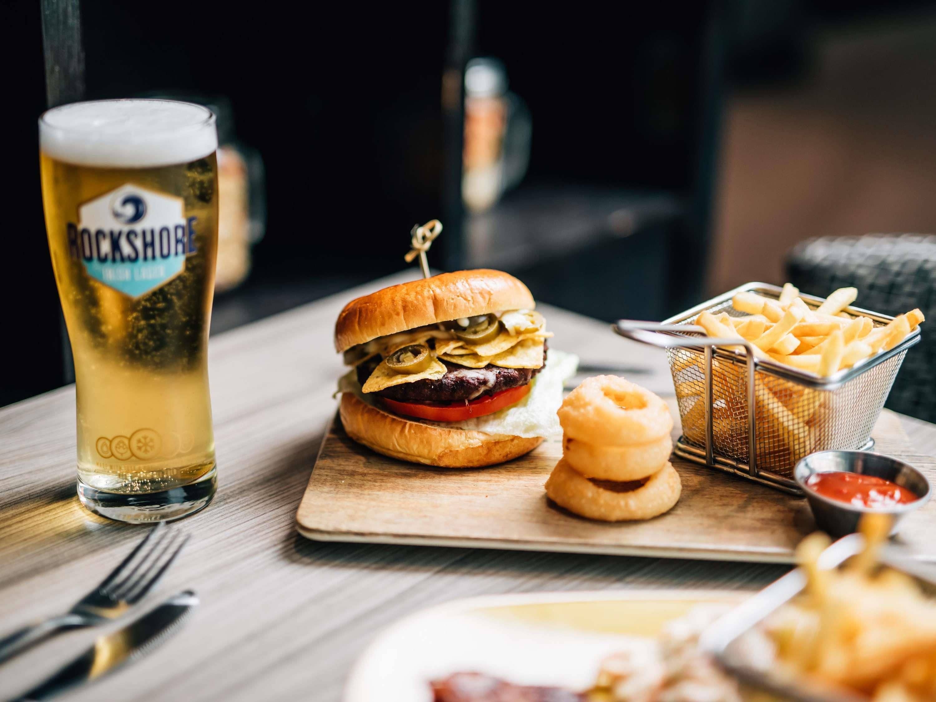 A meal with a burger, fries, onion rings, and a beer glass on a wooden table.