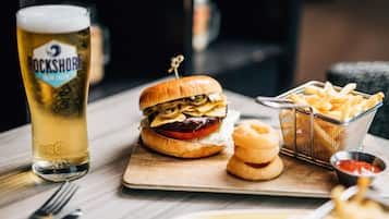 Uma refeição com hambúrguer, batatas fritas, anéis de cebola e um copo de cerveja sobre uma mesa de madeira.
