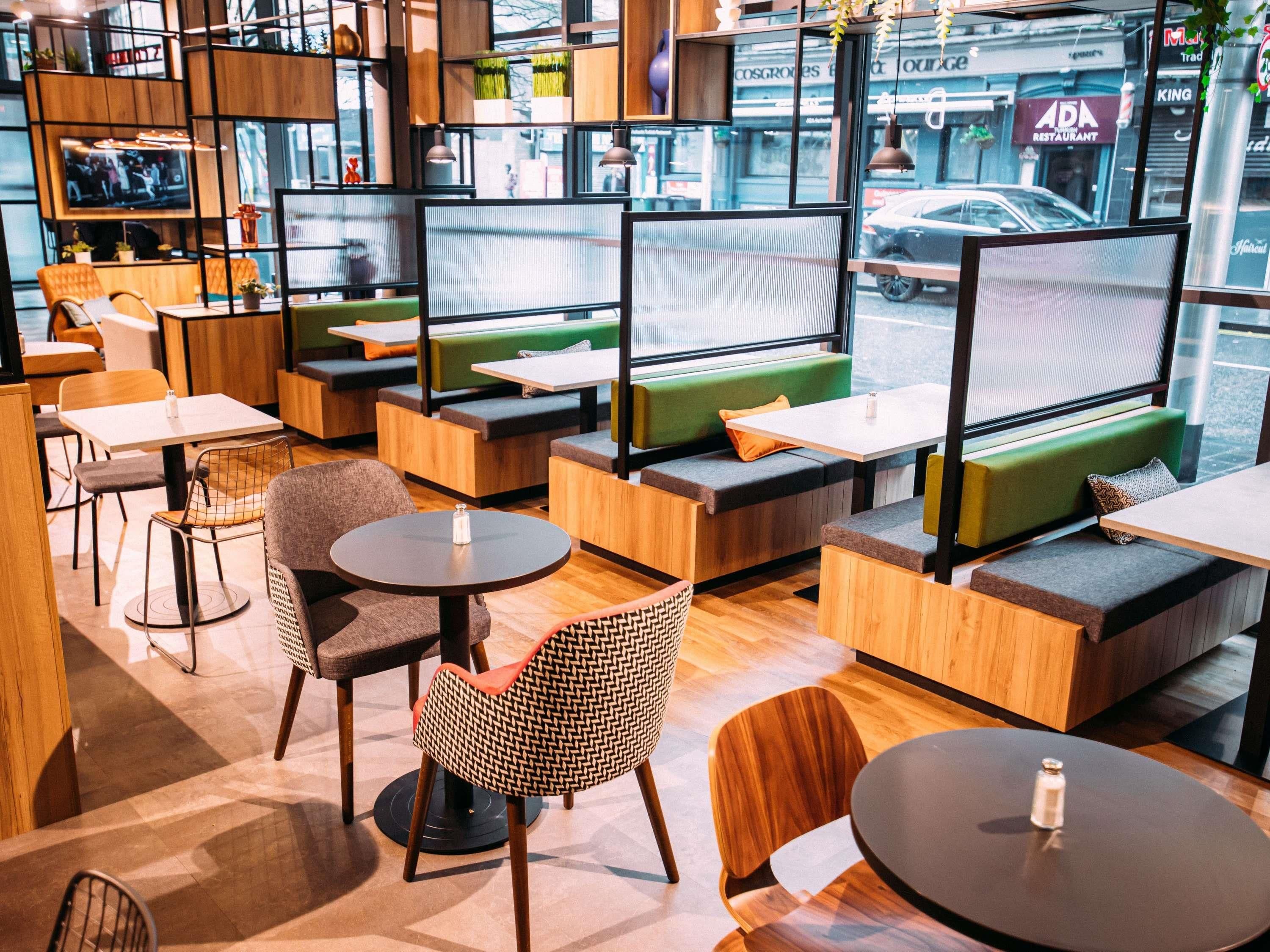 A modern cafe with wooden furniture, green cushioned seating, and a TV screen.
