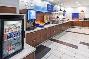 Un espace moderne dédié au petit-déjeuner, équipé d’un réfrigérateur où sont exposés des yaourts et du lait, d’un panier de fruits et d’une machine à café.