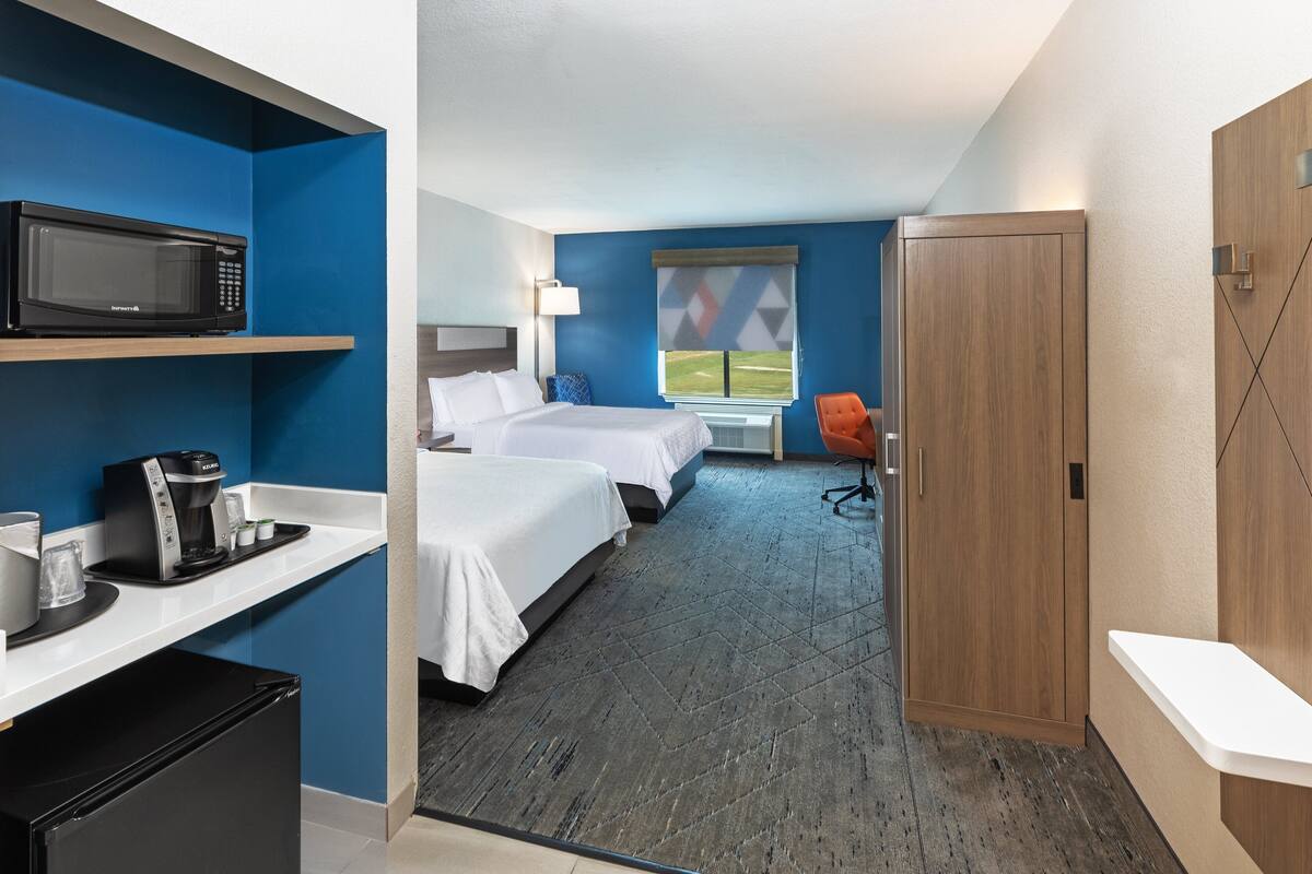 A hotel room with two beds, a microwave, a coffee maker, and a view of a field through the window.