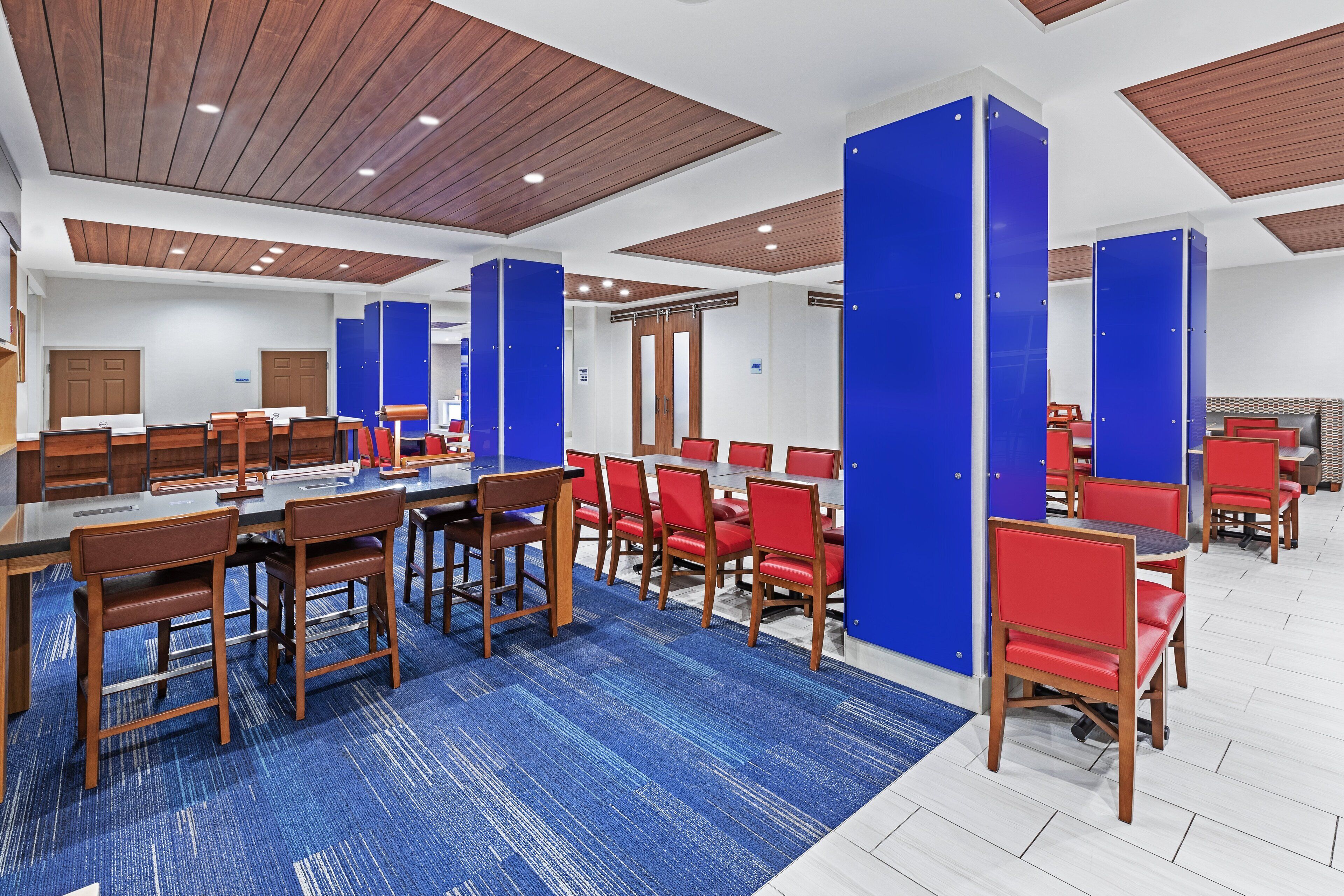 Um saguão de hotel com várias áreas de refeições, painéis de teto de madeira e paredes com detalhes em azul.