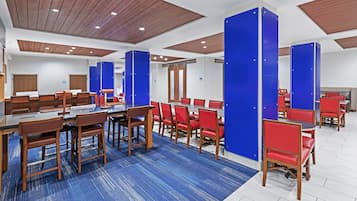 Um saguão de hotel com várias áreas de refeições, painéis de teto de madeira e paredes com detalhes em azul.
