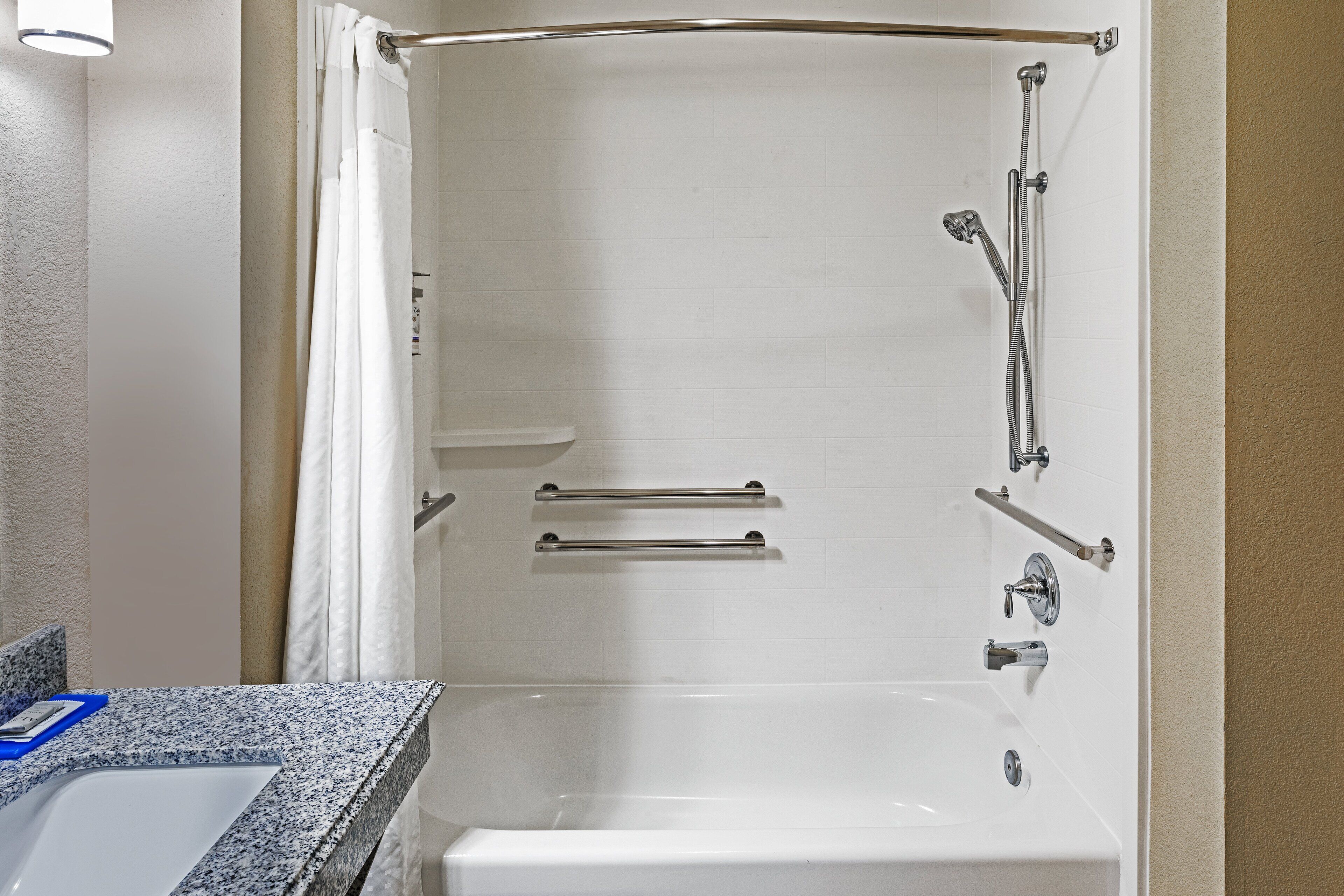 A bathroom with a bathtub, a shower, and a toilet. There are grab bars installed for safety.