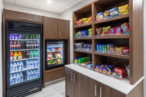 A snack and beverage area with refrigerated drinks and shelves stocked with various snacks and bottled water.
