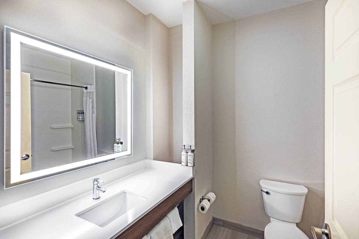 A bathroom with a large mirror, white sink, and toilet.
