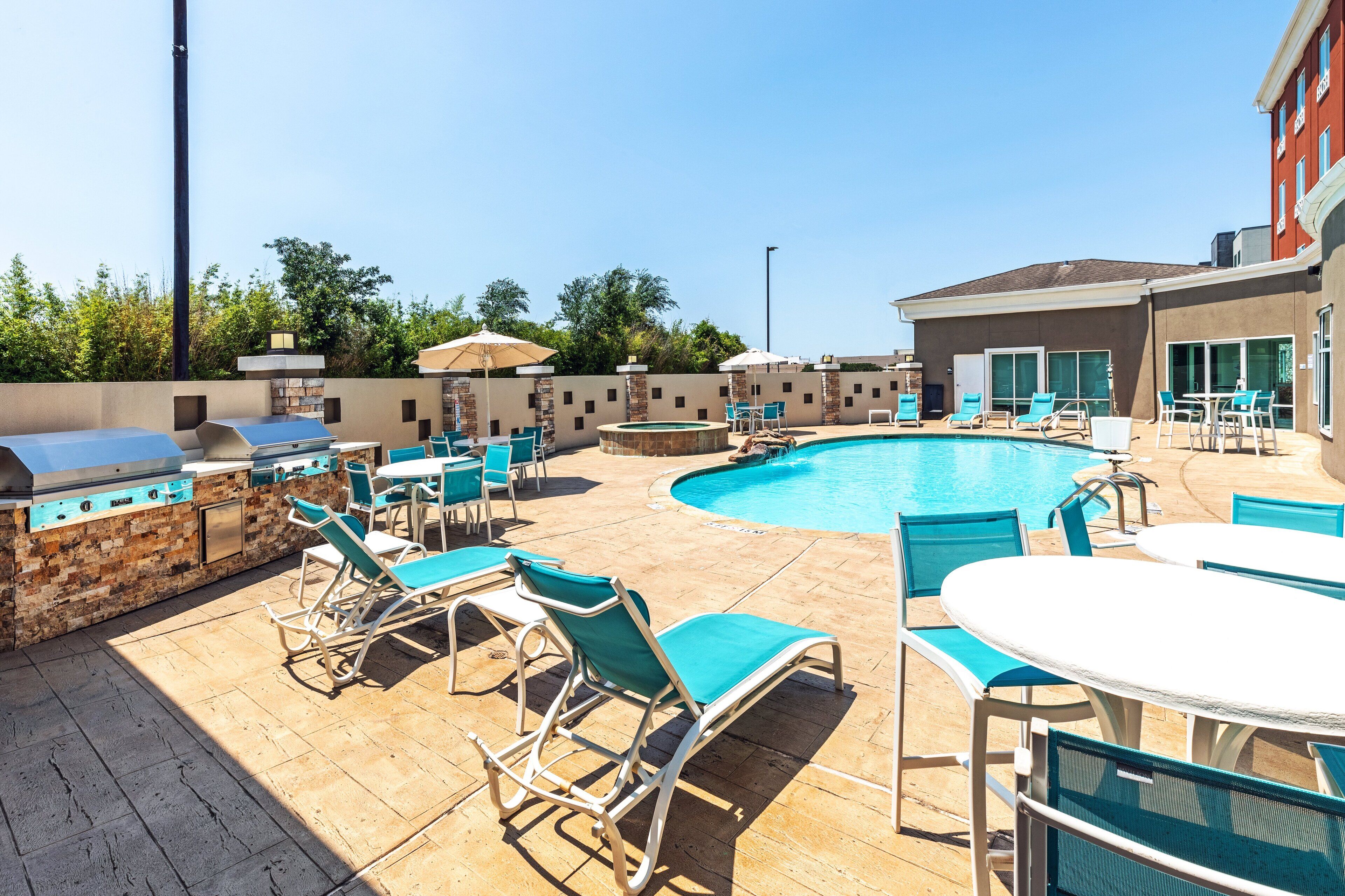 An outdoor pool area with lounge chairs, a barbecue grill, and a table.