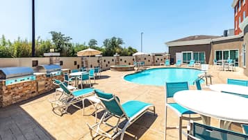 An outdoor pool area with lounge chairs, a barbecue grill, and a table.