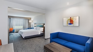 Quarto de hotel com uma cama, um sofá azul, uma mesa de centro de madeira, uma escrivaninha e uma cadeira.