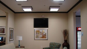 A hotel lobby with a sofa, armchair, a coffee table, a flat-screen TV mounted on the wall, and a Coca-Cola refrigerator. - Holiday Inn Express Hotel & Suites Brownfield by IHG (Brownfield)
