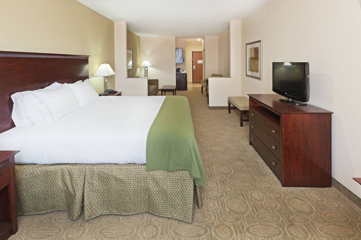 A hotel room with a large bed, a television, a desk, and a chair.