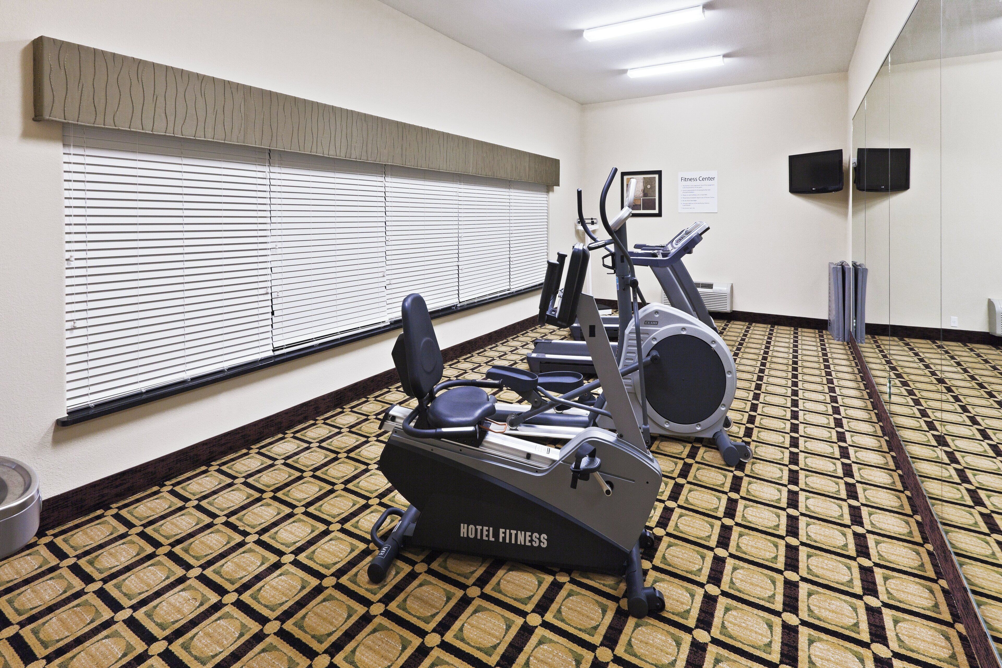 A hotel fitness center with exercise equipment, a patterned carpet, and a sign indicating the room's purpose.