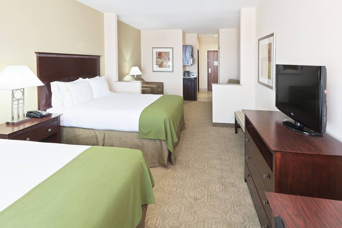 A hotel room with two beds, a TV, a desk, and a small kitchenette.