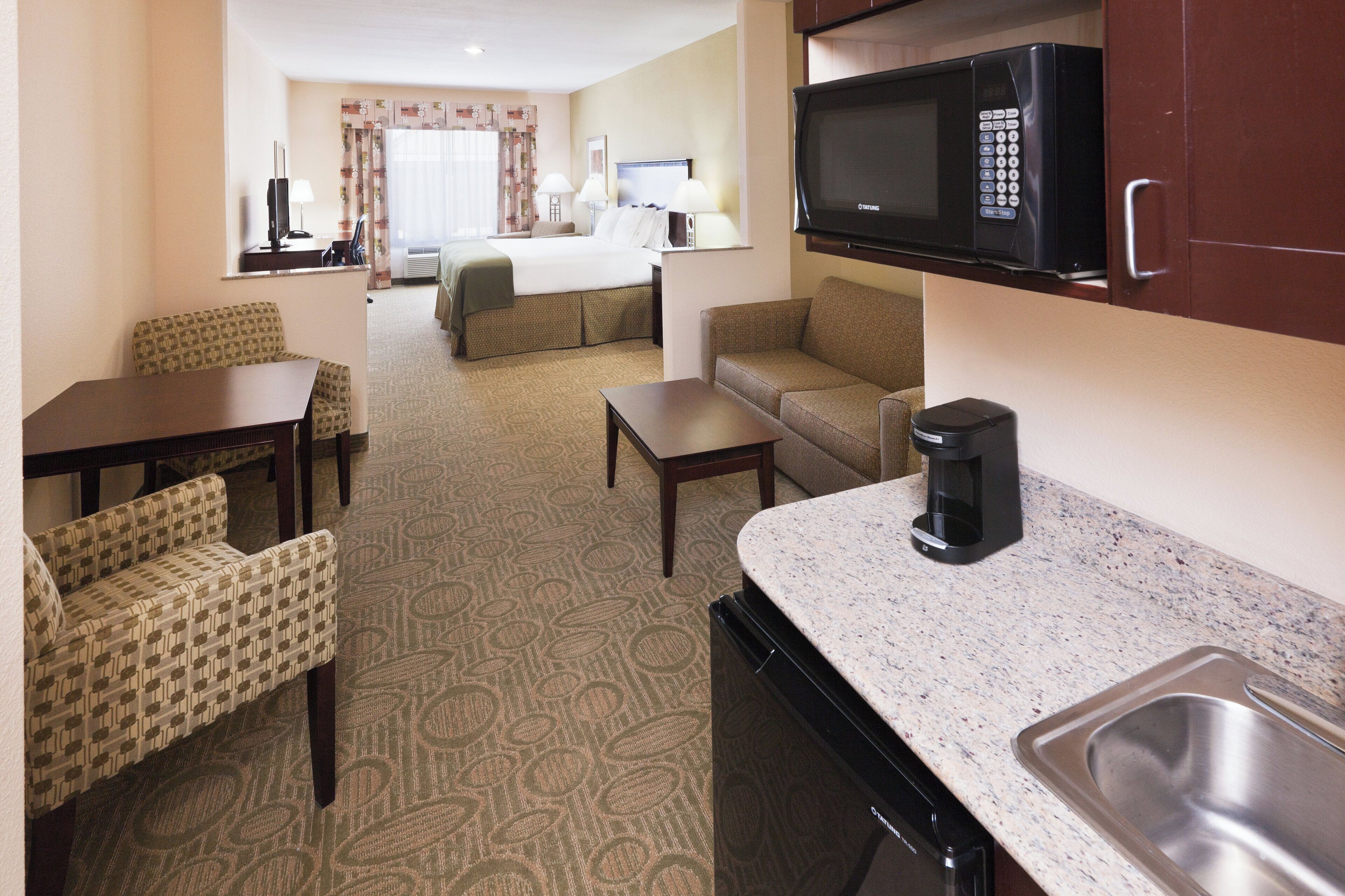 A hotel room with a kitchenette, a bed, a sofa, a dining table, and a coffee maker.