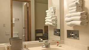 A bathroom with a sink, mirror, towel rack, and a door leading to another room. - Holiday Inn Express Hotel & Suites Brownfield by IHG (Brownfield)
