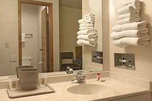 Un baño con lavamanos, espejo, toallero y puerta que da a otra habitación.