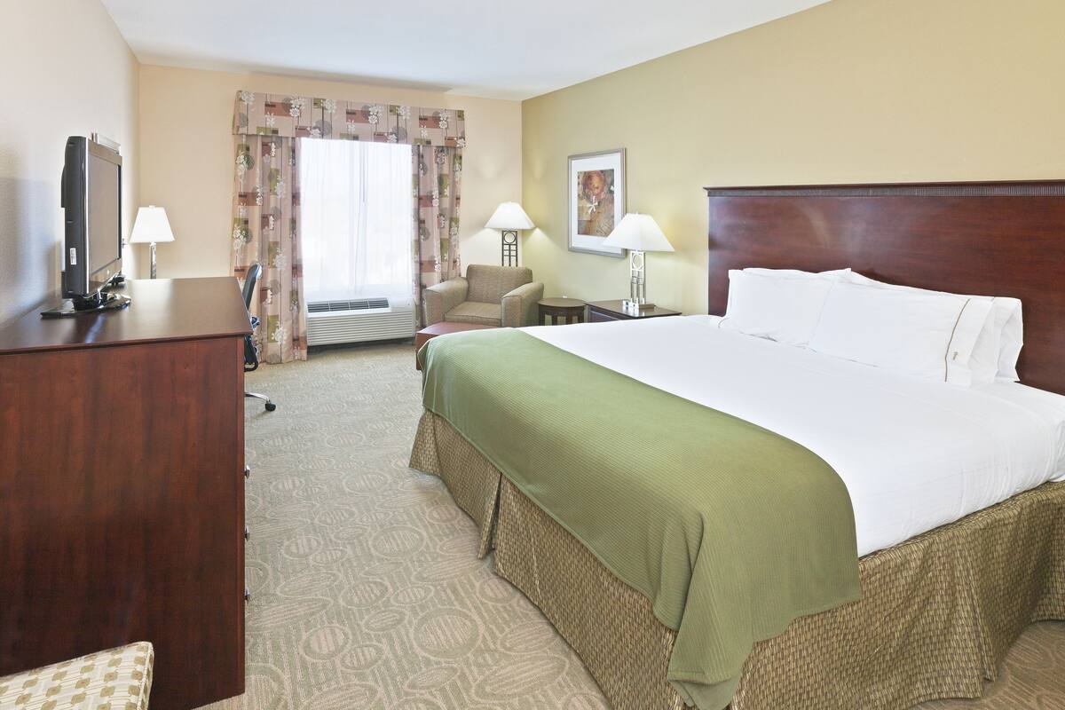 A hotel room with a large bed, a desk with a computer, a chair, two lamps, and a window with curtains.
