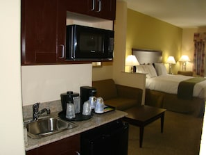 Una habitación de hotel compacta con kitchenette, una cama y un pequeño espacio de descanso.