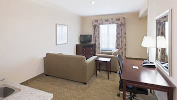 A hotel room with a sofa, a small table, a desk with a telephone, a television, a mirror, and a window with curtains.