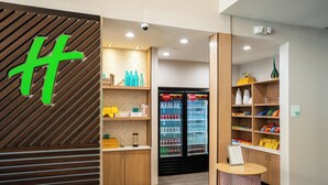 Un vestíbulo de hotel moderno con paneles de madera, un refrigerador Coca-Cola, estantes con snacks y un mostrador de recepción.
