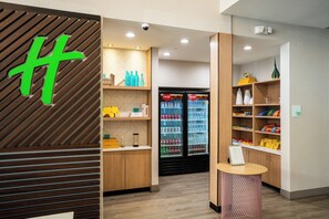A modern hotel lobby with wooden paneling, a Coca-Cola refrigerator, snack shelves, and a reception desk. - Holiday Inn Hou Energy Corridor Eldridge by IHG (Houston)