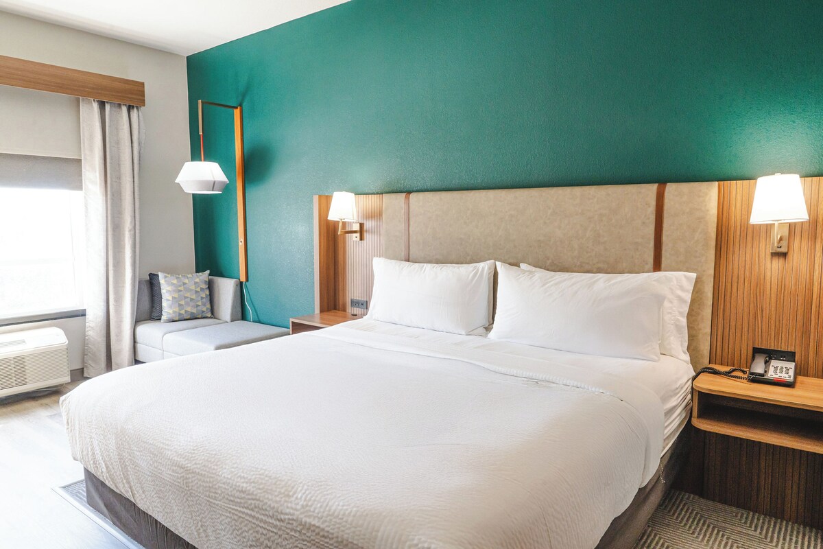 A hotel room with a large bed, bedside lamps, a small seating area, and a window with curtains.