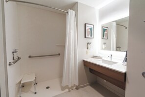 A modern bathroom with a walk-in shower, grab bars, a small step stool, a sink, and a mirror. - Holiday Inn Hou Energy Corridor Eldridge by IHG (Houston)