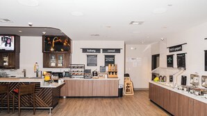 Un café moderno con un mostrador central, zona de bar, panadería y estación de fruta y yogur.