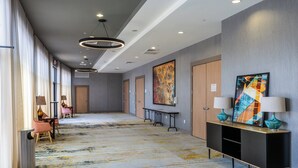 Un pasillo de hotel con diseño moderno, que presenta un largo corredor, una recepción y un cuadro abstracto grande en la pared.
