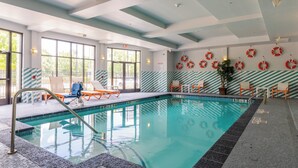 Una piscina interior con agua cristalina, una silla de salvavidas y sillas de descanso.