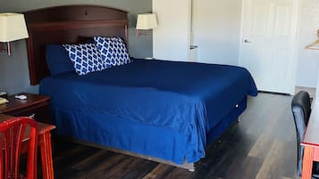 Camera d'albergo con un letto grande, testiera in legno, due lampade ai lati del letto, una scrivania con una sedia e una porta.