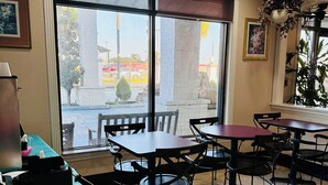 A restaurant interior with a large window, tiled floor, and several tables and chairs. - Magnolia Inn And Suites (Magnolia)