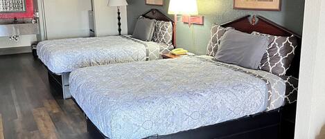 Une chambre d’hôtel avec deux lits, un plancher en bois, un bureau, une chaise, une lampe et un tableau au mur.