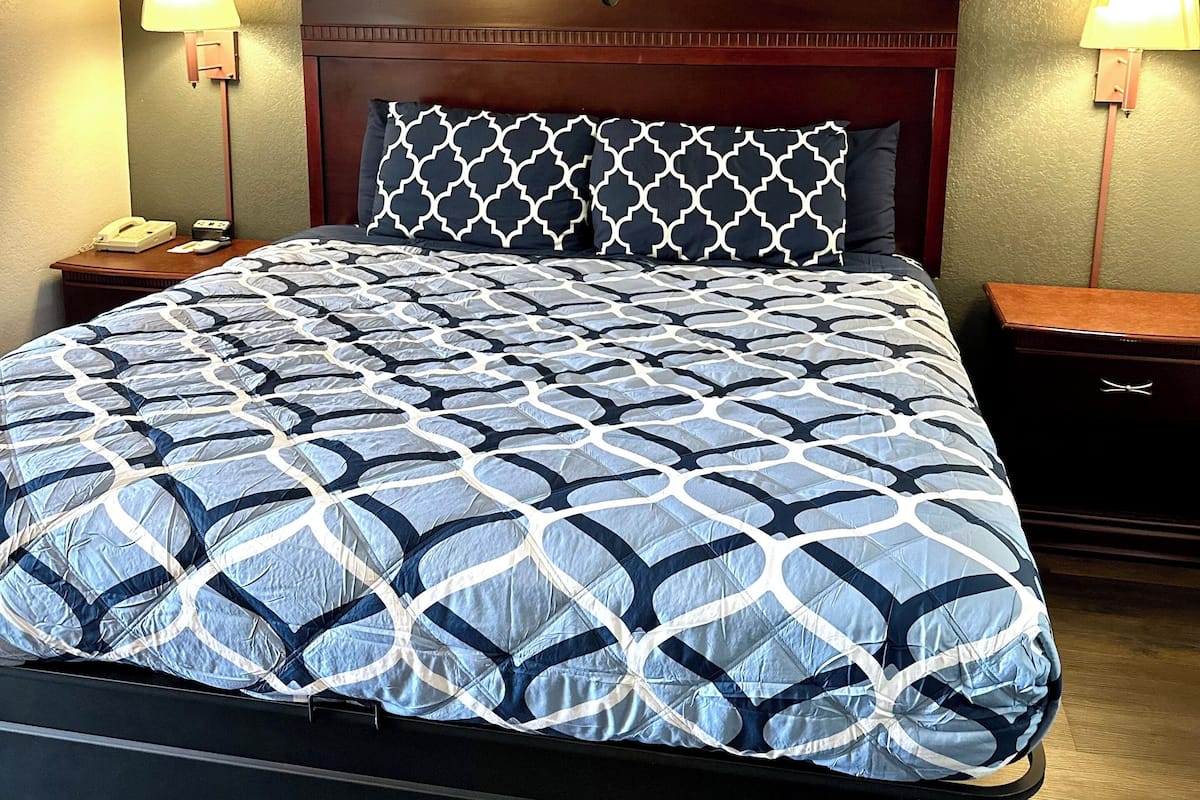 A neatly made bed with a patterned bedspread, a wooden headboard, and two bedside lamps.