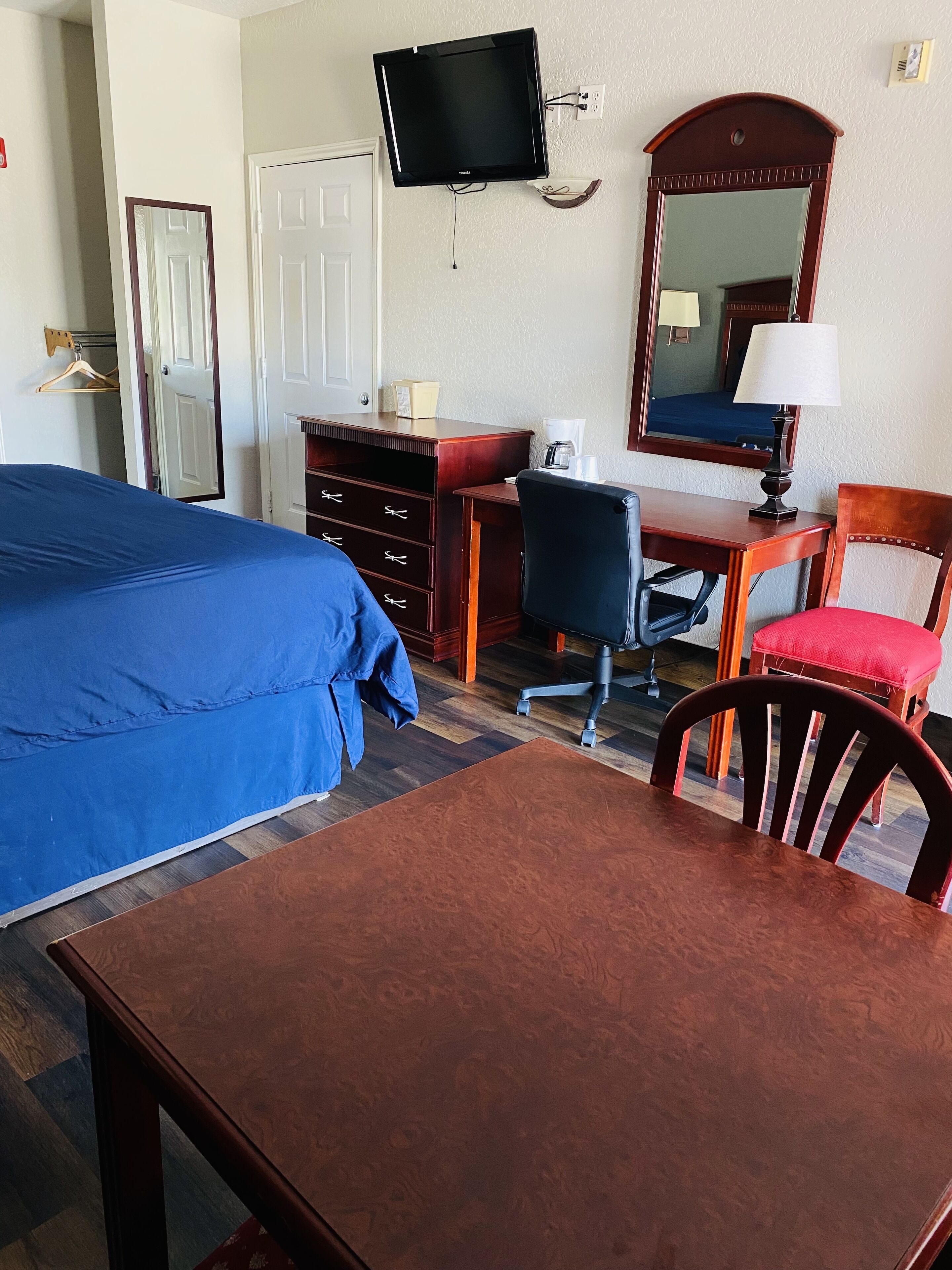 Habitación de hotel con cama, escritorio, silla, televisor y espejo.