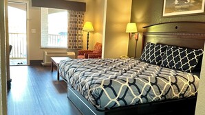 A hotel room with a large bed, two bedside lamps, a window with curtains, a chair, and a door leading to a balcony. - Magnolia Inn And Suites (Magnolia)