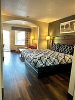 Habitación de hotel con una cama grande, dos lámparas de noche, una ventana con cortinas, una silla y una puerta que da a un balcón.