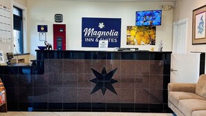 A hotel reception area with a large sign for Magnolia Inn & Suites, a digital clock, a TV mounted on the wall, and a tiled floor. - Magnolia Inn And Suites (Magnolia)