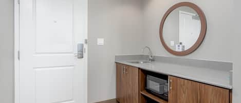A modern bathroom with a white door, a wooden vanity with a sink, and a microwave.