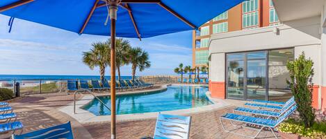 A poolside area with lounge chairs, a table, and a large umbrella.