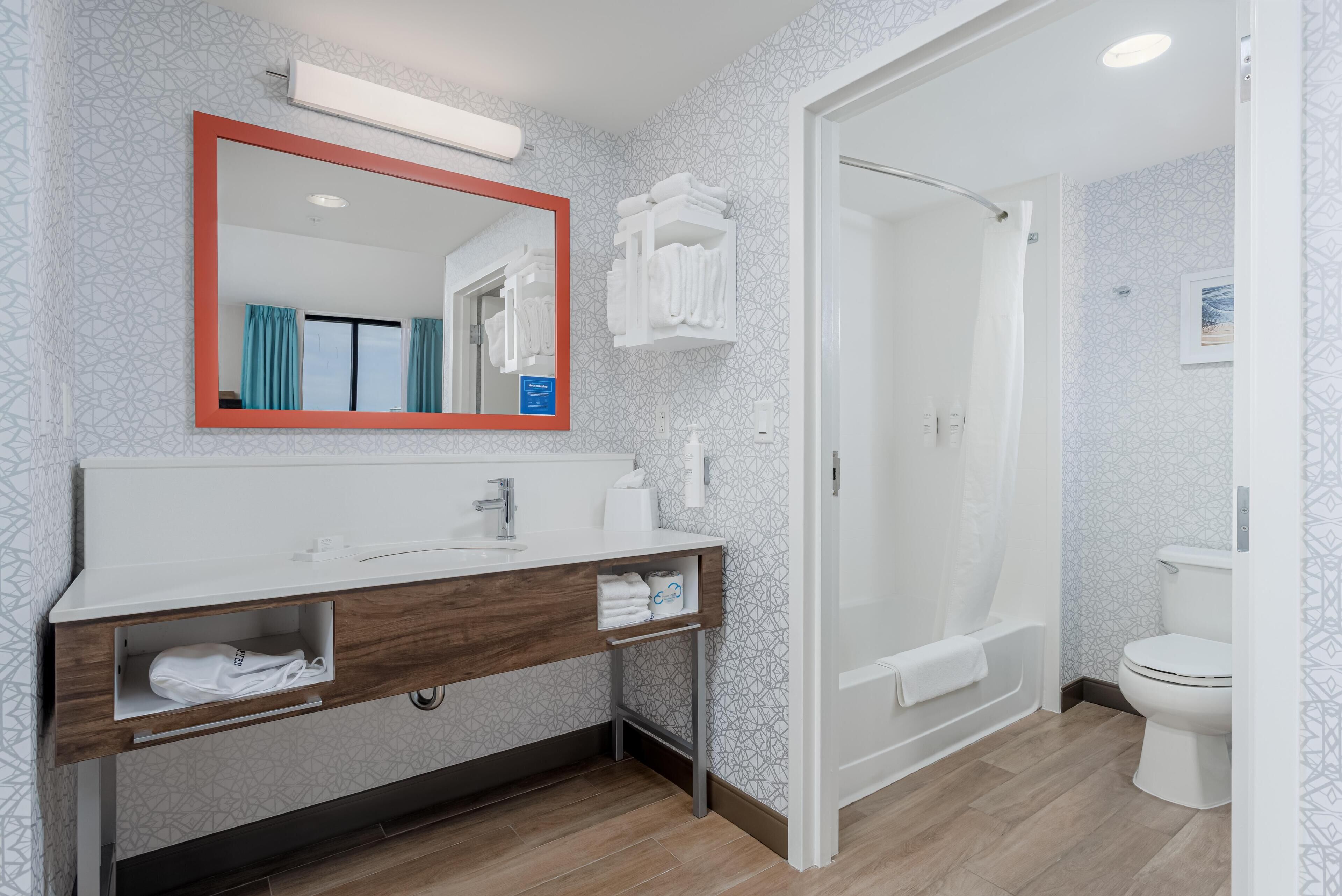 A modern bathroom with a large mirror, white sink, and shower.