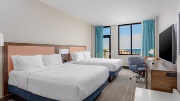 Habitación de hotel con dos camas, un escritorio, una silla, un televisor y un ventanal con vistas al mar.