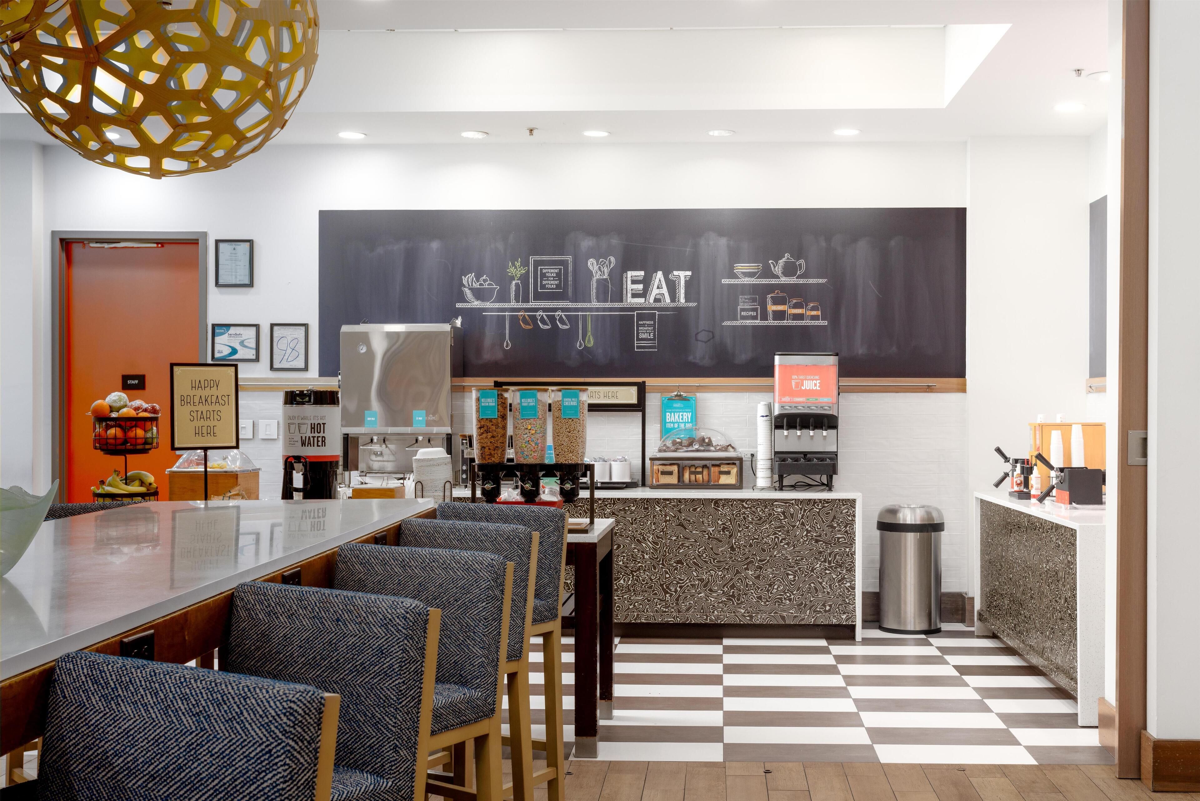 A modern cafe with a checkered floor, a chalkboard menu, and seating areas.