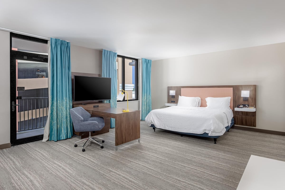A hotel room with a bed, desk, chair, TV, and a window with curtains.