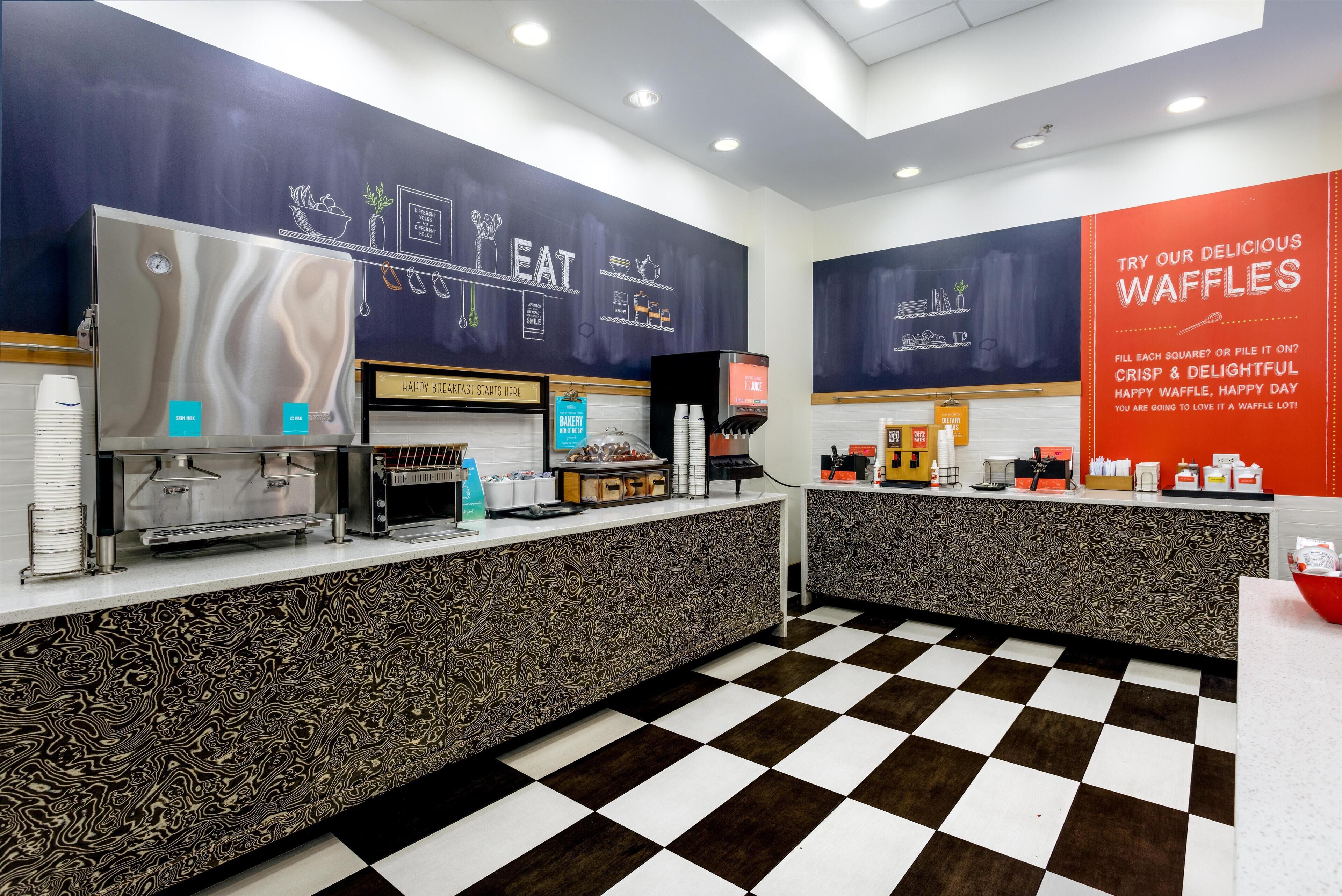 A cafe with a checkered floor, a stainless steel espresso machine, and a menu board.