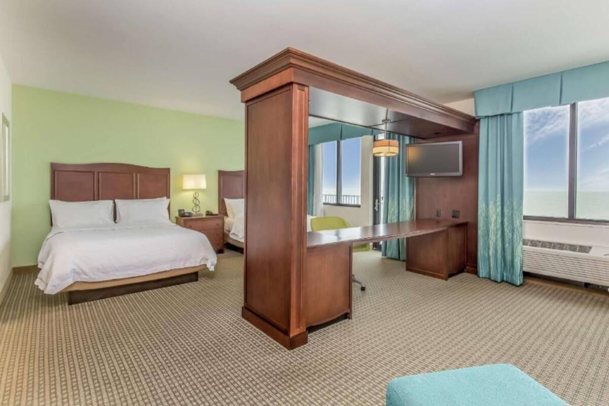 A hotel room with a bed, a desk, a TV, and a large window with a view.